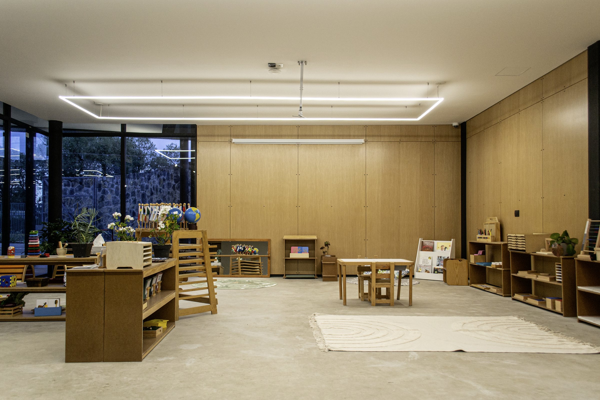 Aula de madera con los muebles bajos y el ventanal al bosque