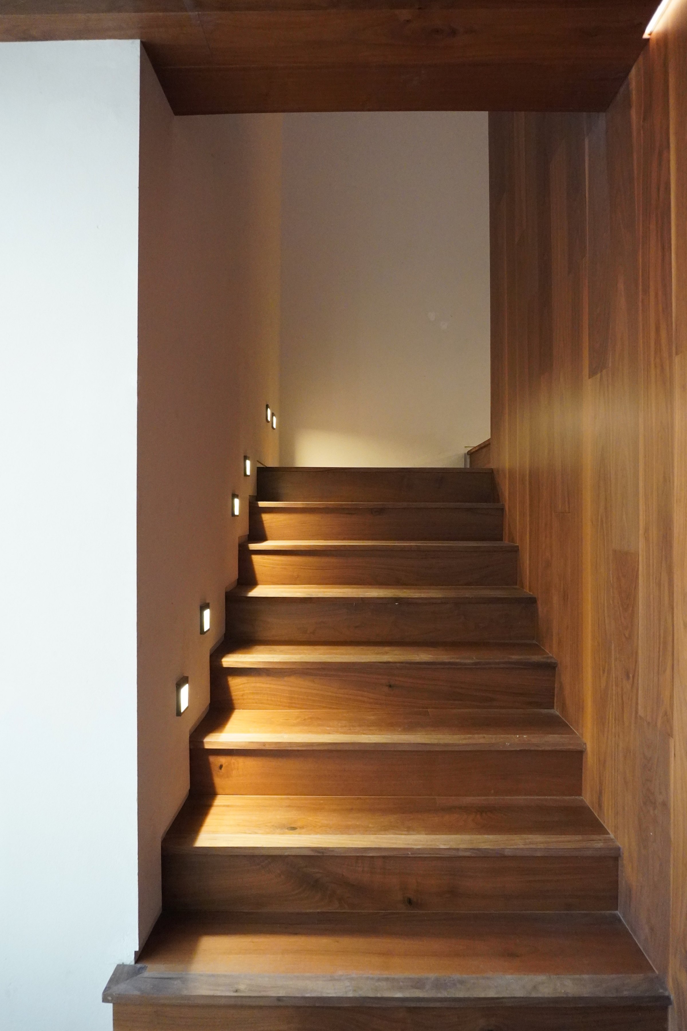 La escalera de peldaños de madera contra el muro iluminado